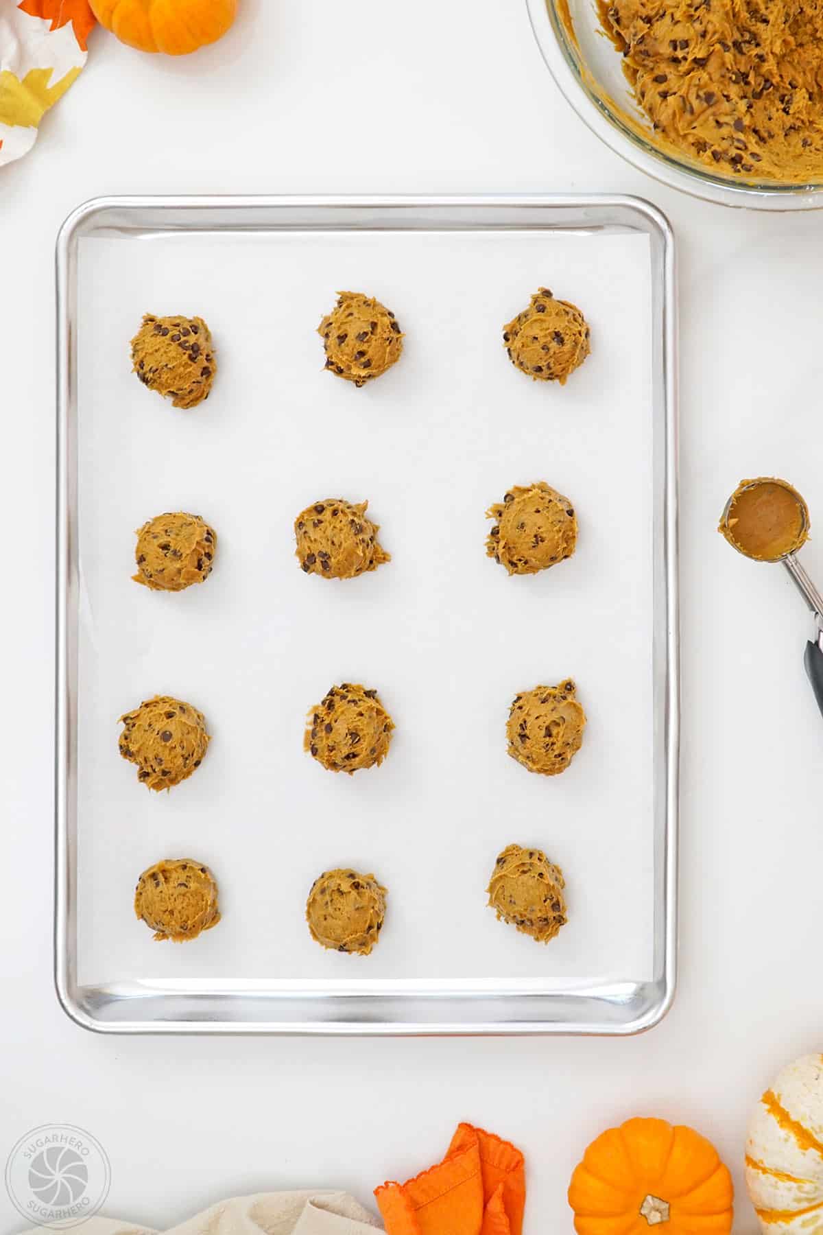 A parchment-lined baking tray with pumpkin chocolate chip cookie dough balls on it.