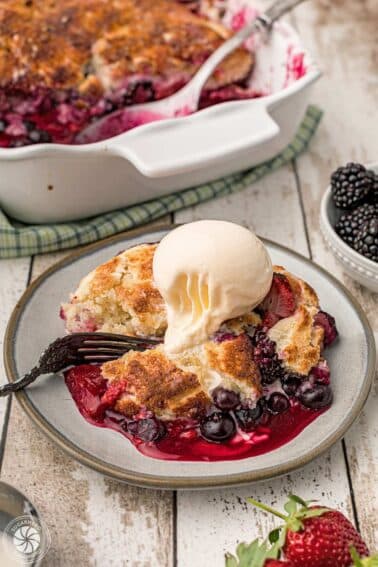 Berry cobbler on a plate with a scoop of ice cream on top.