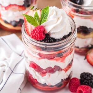 Three jars of mixed berry shortcake with berries, whipped cream, and shortcakes.