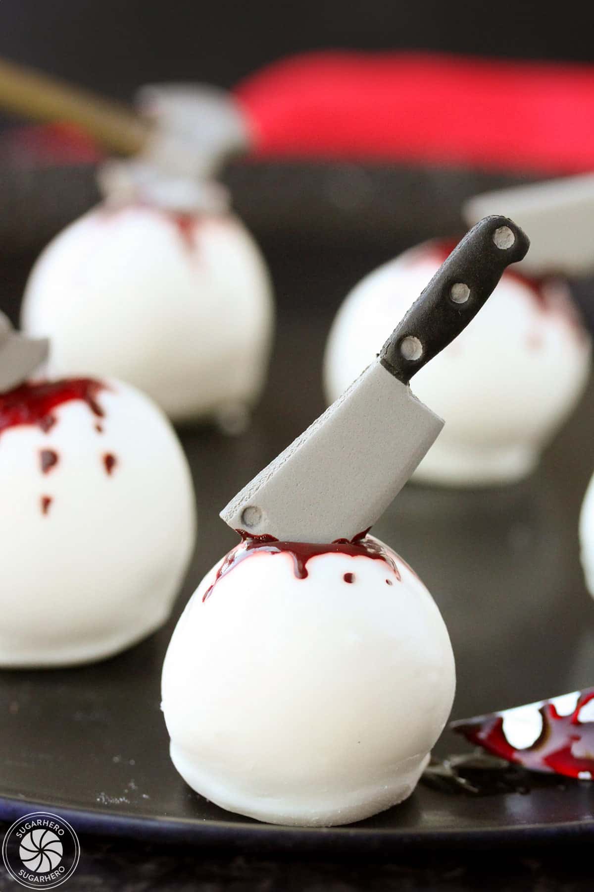 Halloween Cake Ball Truffles on a black plate, decorated with candy weapons and food coloring blood.