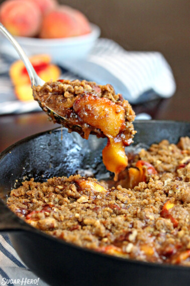 Spoon taking a big scoop of peach cobbler out of a cast iron skillet.