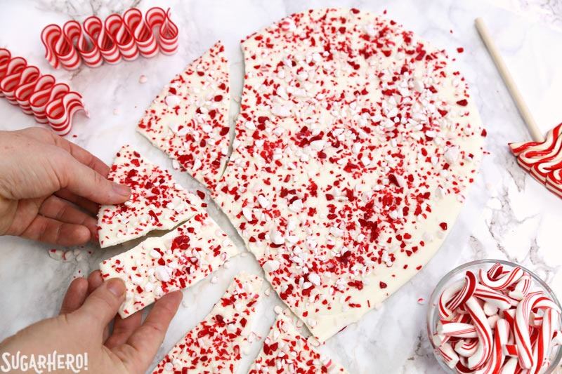 Hands breaking apart peppermint bark with red and white candy scattered on the sides