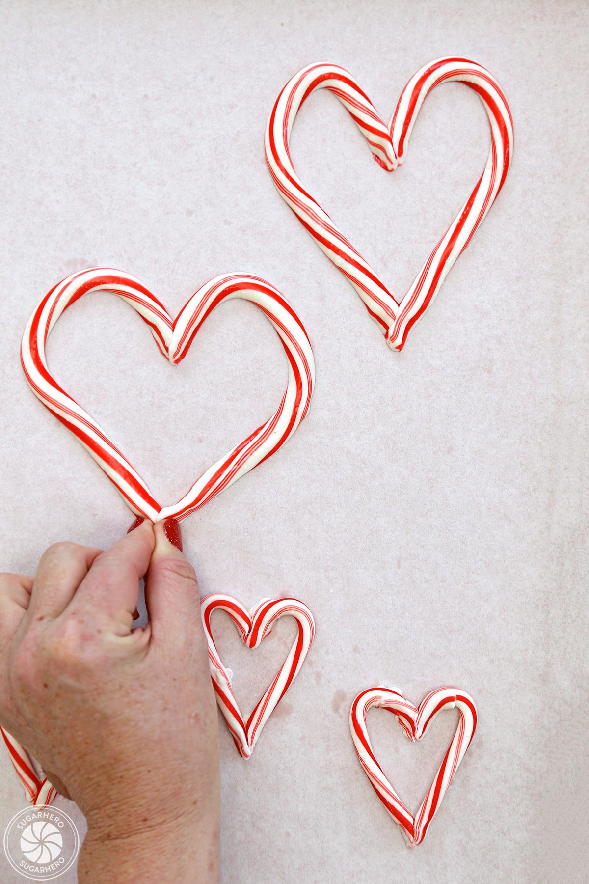 Hand pinching together two candy canes to make a heart shape.