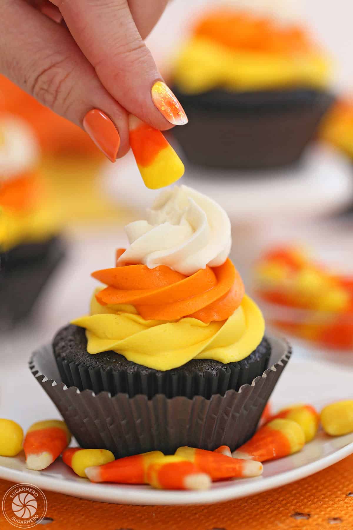 Hand putting a candy corn on top of a frosted Candy Corn Cupcake.