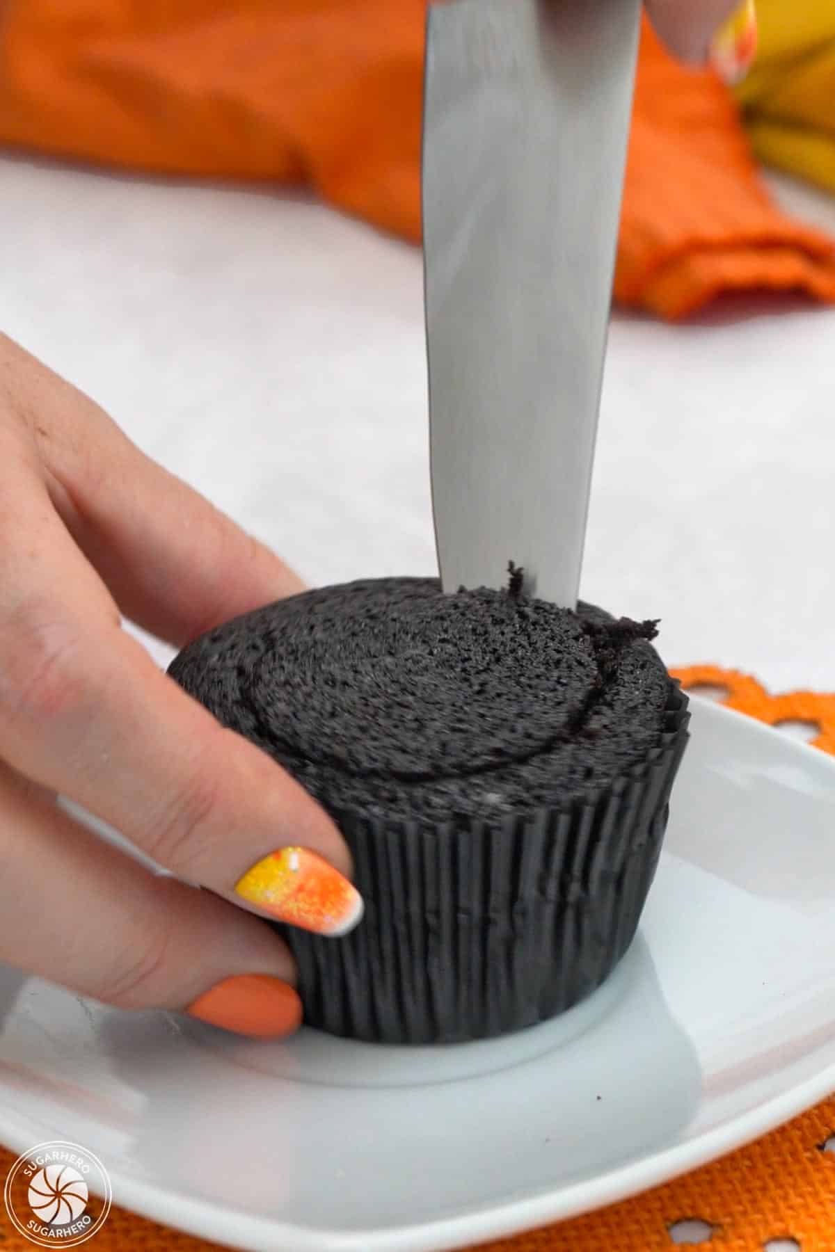 Cutting a cone shape in the top of a chocolate cupcake.