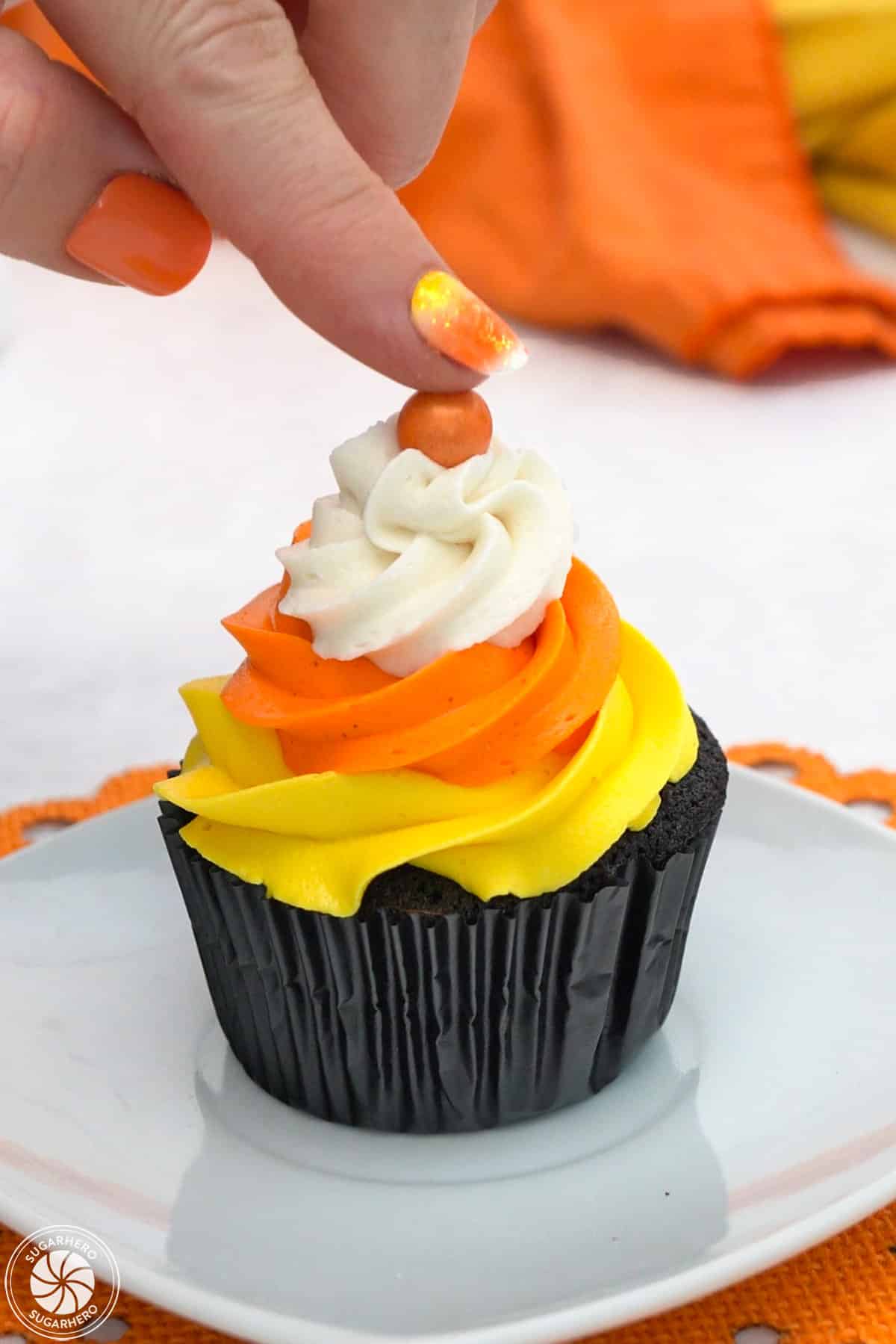 Hand pressing an orange Sixlet on top of a Candy Corn Cupcake.