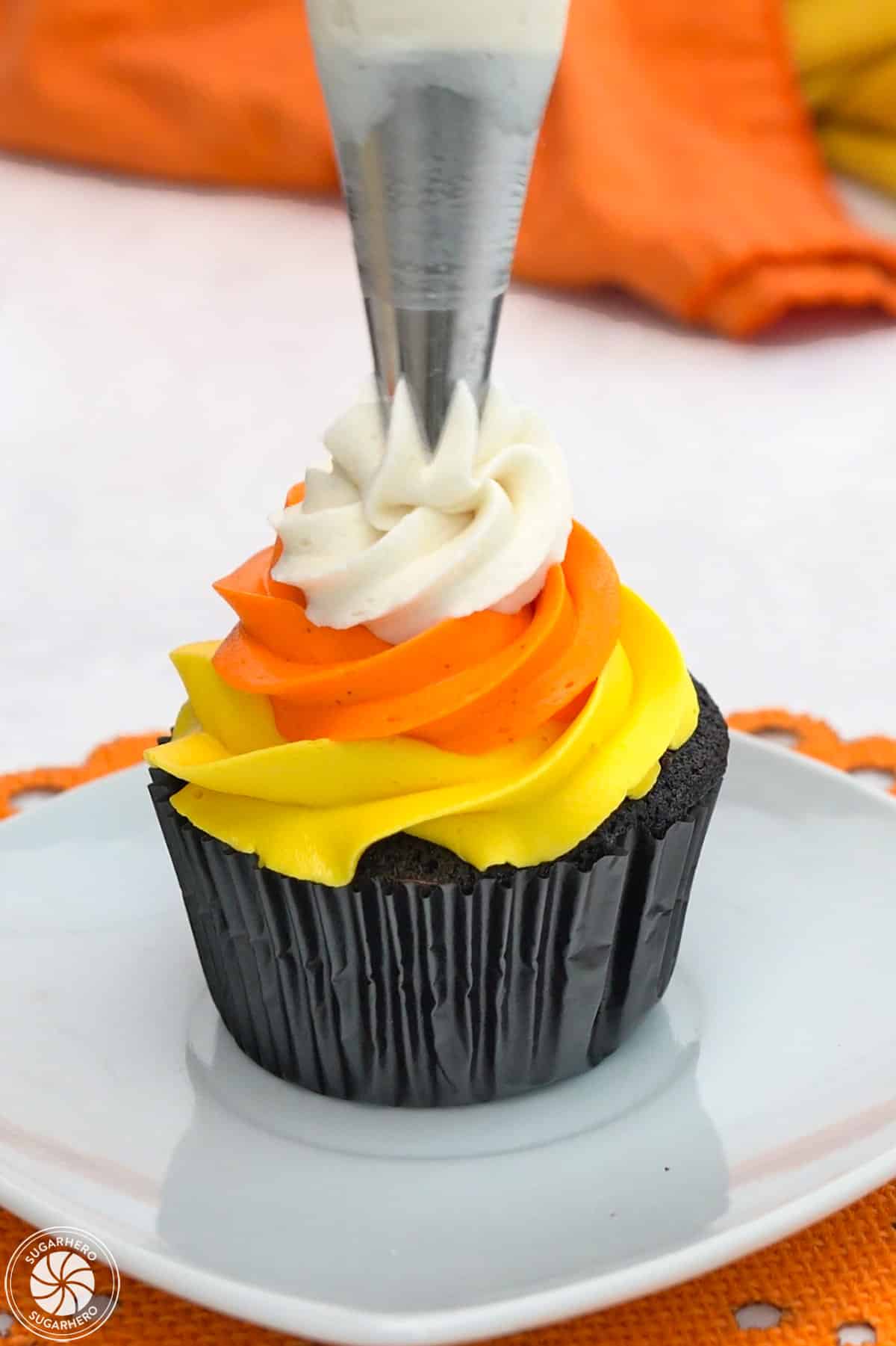 Adding white buttercream on top of a Candy Corn Cupcake.