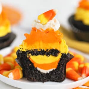 A Candy Corn Cupcake on a white plate, cut in half to show the hidden frosting candy corn inside.