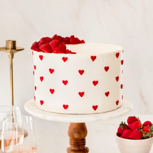 Champagne Strawberry Truffle Cake on a wood and marble cake platter with champagne and strawberries below the cake.