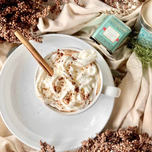 Cup of Chocolate Chai Latte on a white plate with an inserted cinnamon stick.