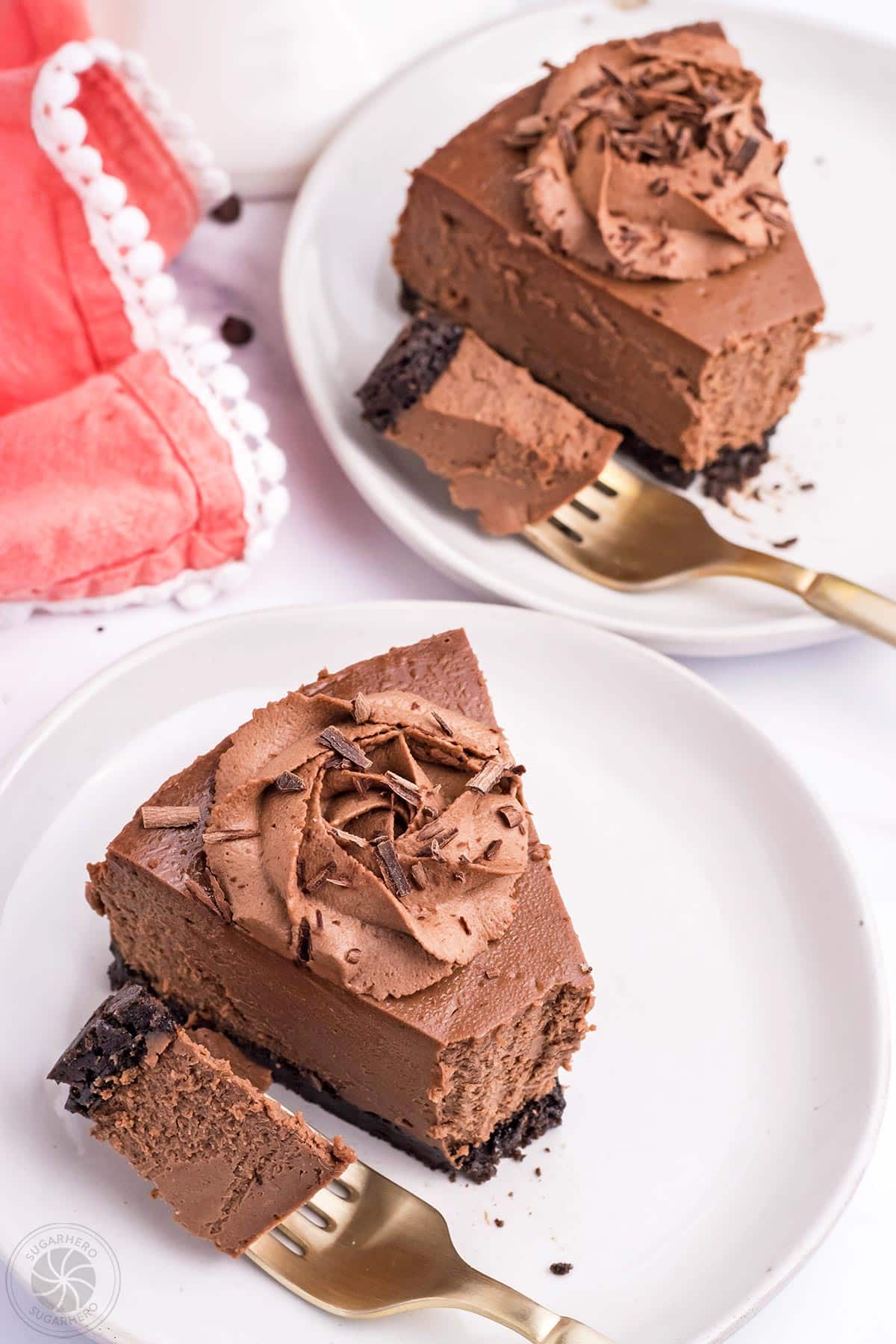 2 slices of Chocolate Cheesecake on white plates with forks holding bites of cheesecake to show texture.