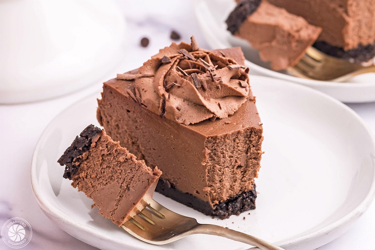 A slice of Chocolate Cheesecake on a white plate with a bite on a fork.