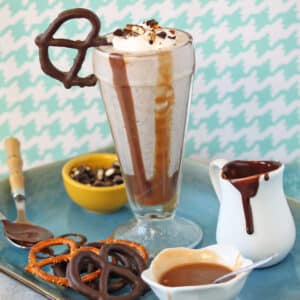 Chocolate Covered Pretzel Milkshake on a tray next to pretzels and dessert sauces.