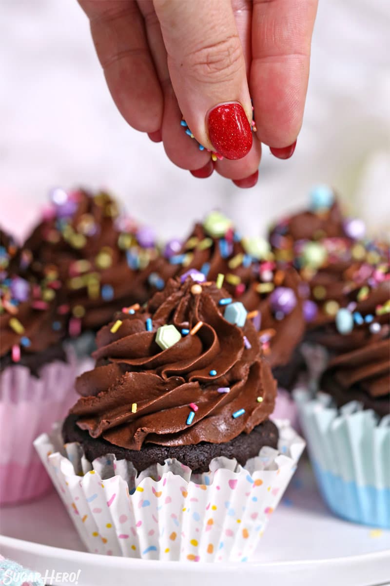 Sprinkling colorful sprinkles on top of a frosted chocolate cupcake