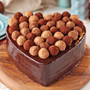 Heart-shaped cake covered in chocolate glaze, with truffles on top.