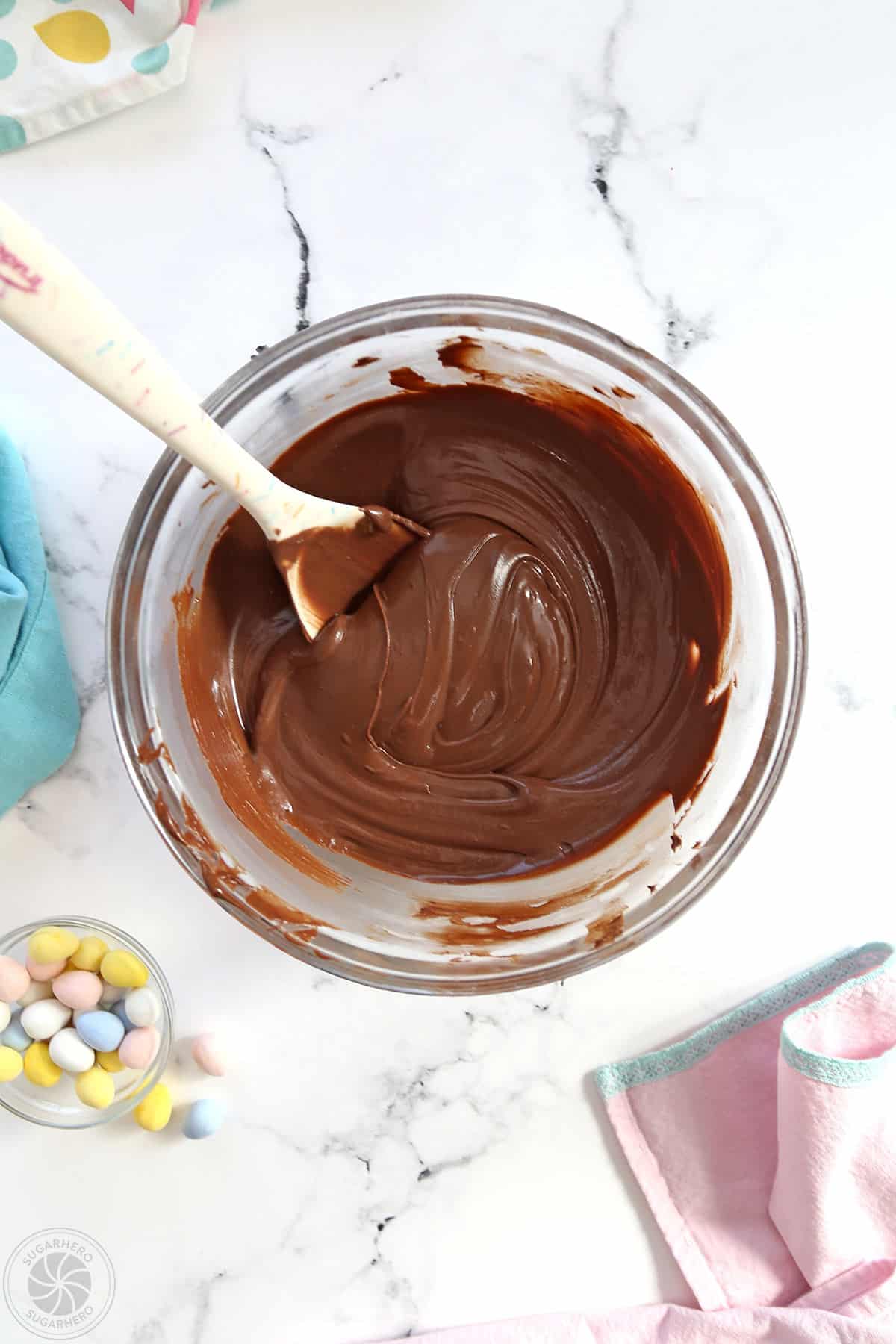 Chocolate, melted in a large glass bowl, with a silicone spatula sticking out of it.