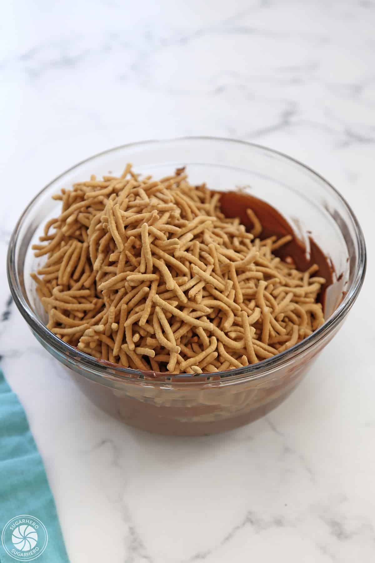 Chow mein noodles added to melted chocolate in a glass bowl.