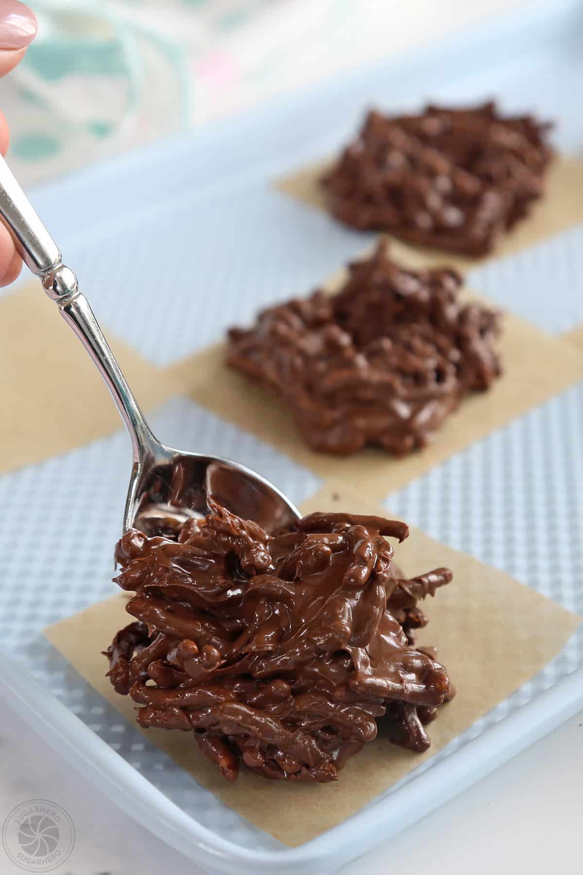 Spooning chocolate-coated chow mein noodles onto parchment squares.