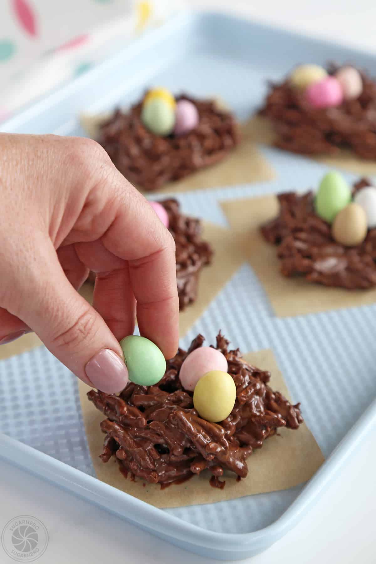 Placing candy eggs in the center of chocolate nests.