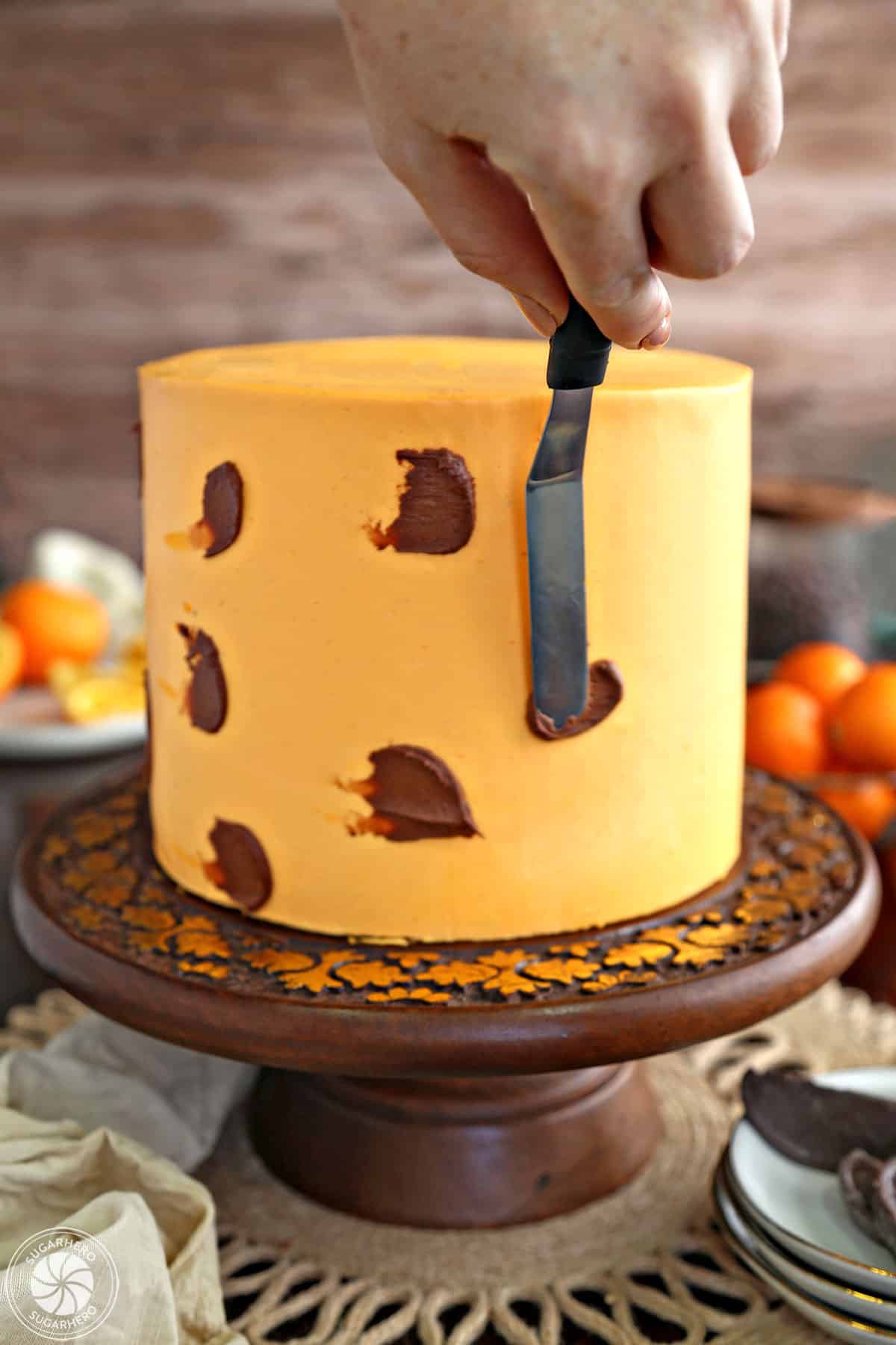 Using a spatula to put dabs of chocolate frosting on the outside of a chocolate orange cake frosted with orange buttercream.