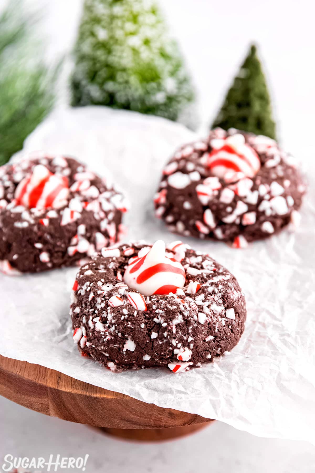 3 Chocolate Peppermint Kiss Cookies on a piece of parchment with evergreen trees in the background.