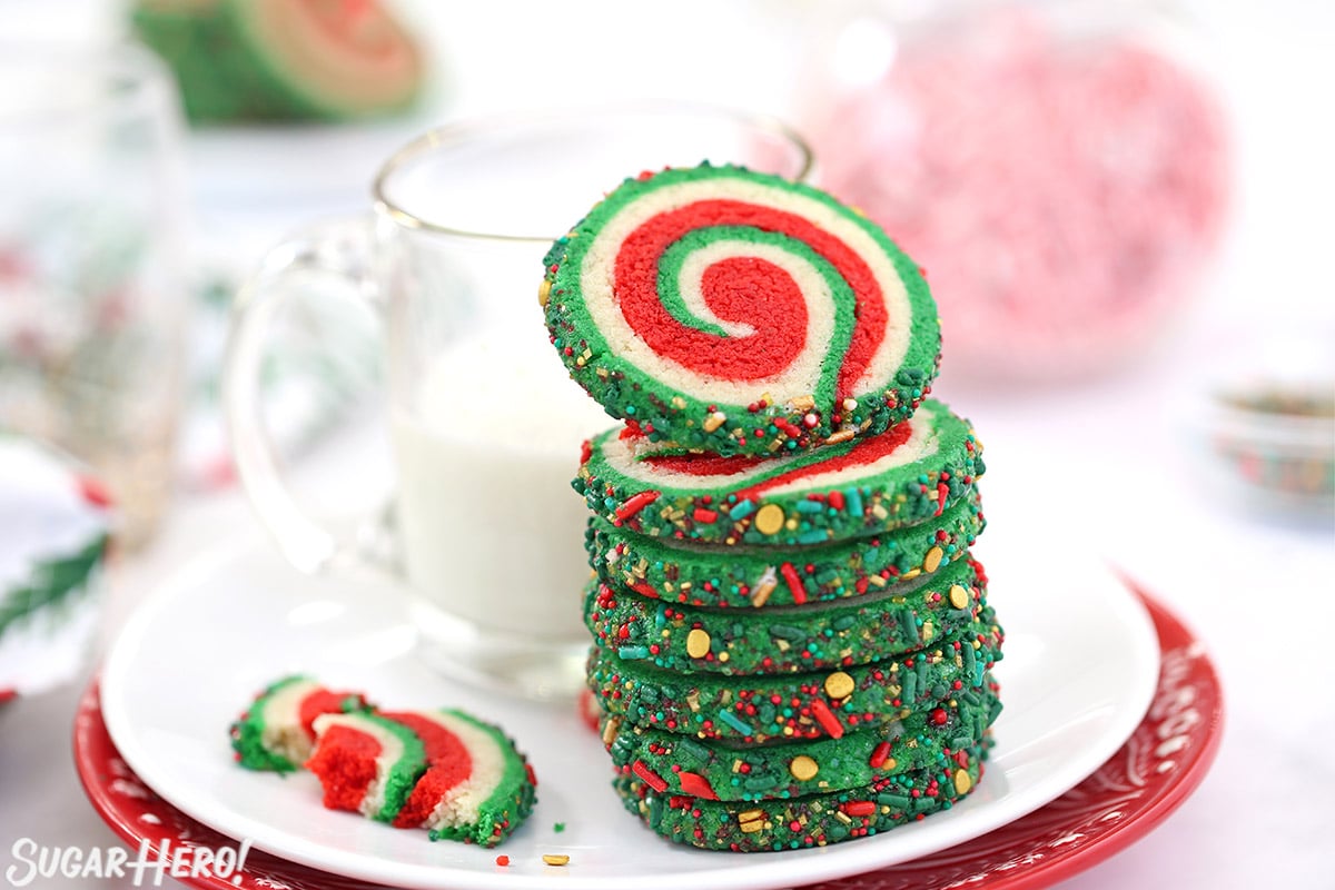 Stack of red, white, and green Christmas pinwheel cookies and a mug of milk.