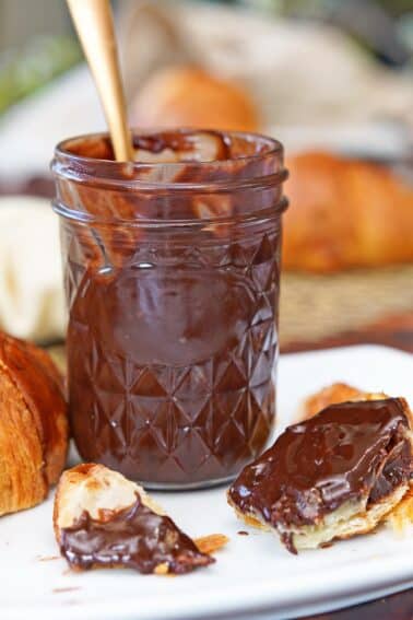 A jar of Coconut Chocolate Spread with some covered pieces of croissant below it.