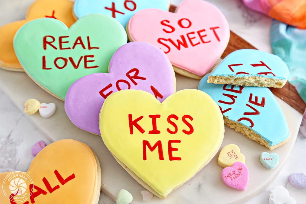 Several Conversation Heart Sugar Cookies stacked on a cutting board.