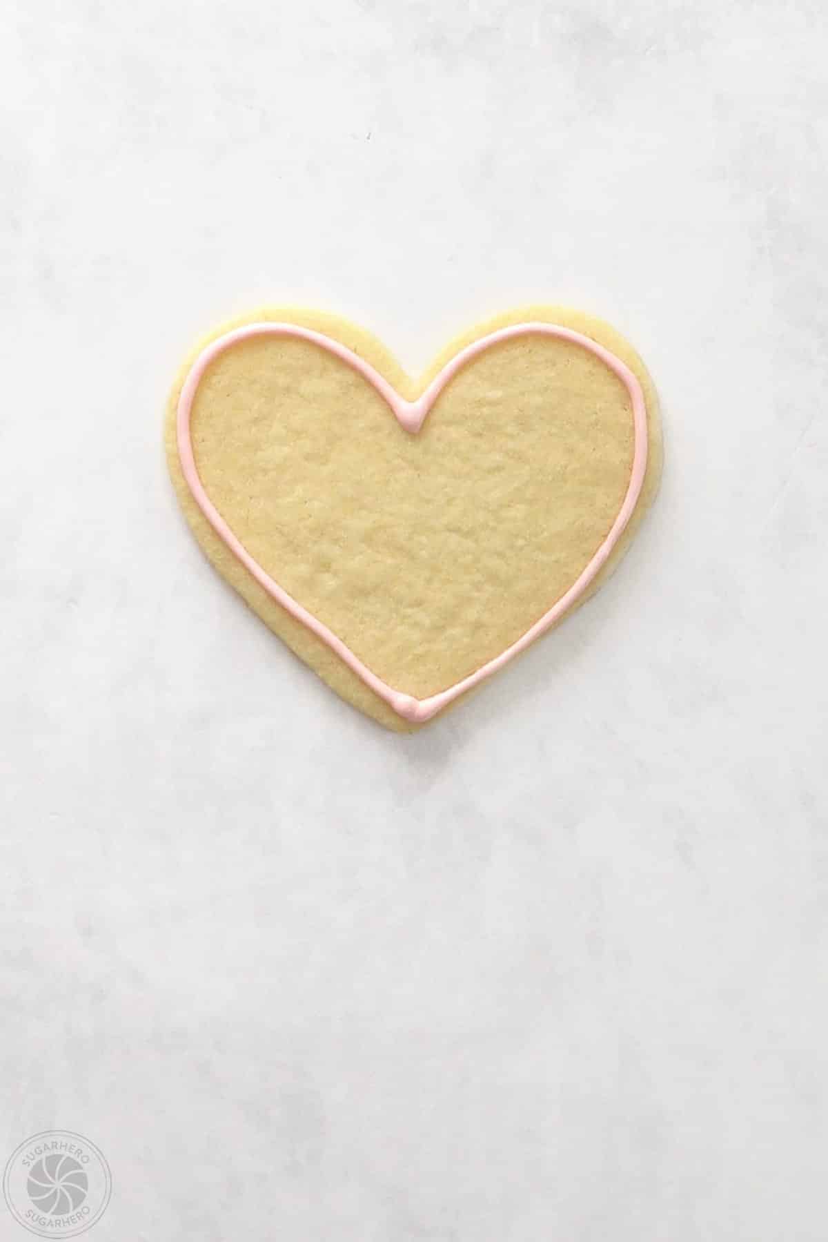 A heart shaped sugar cookie that has been outlined with royal icing.