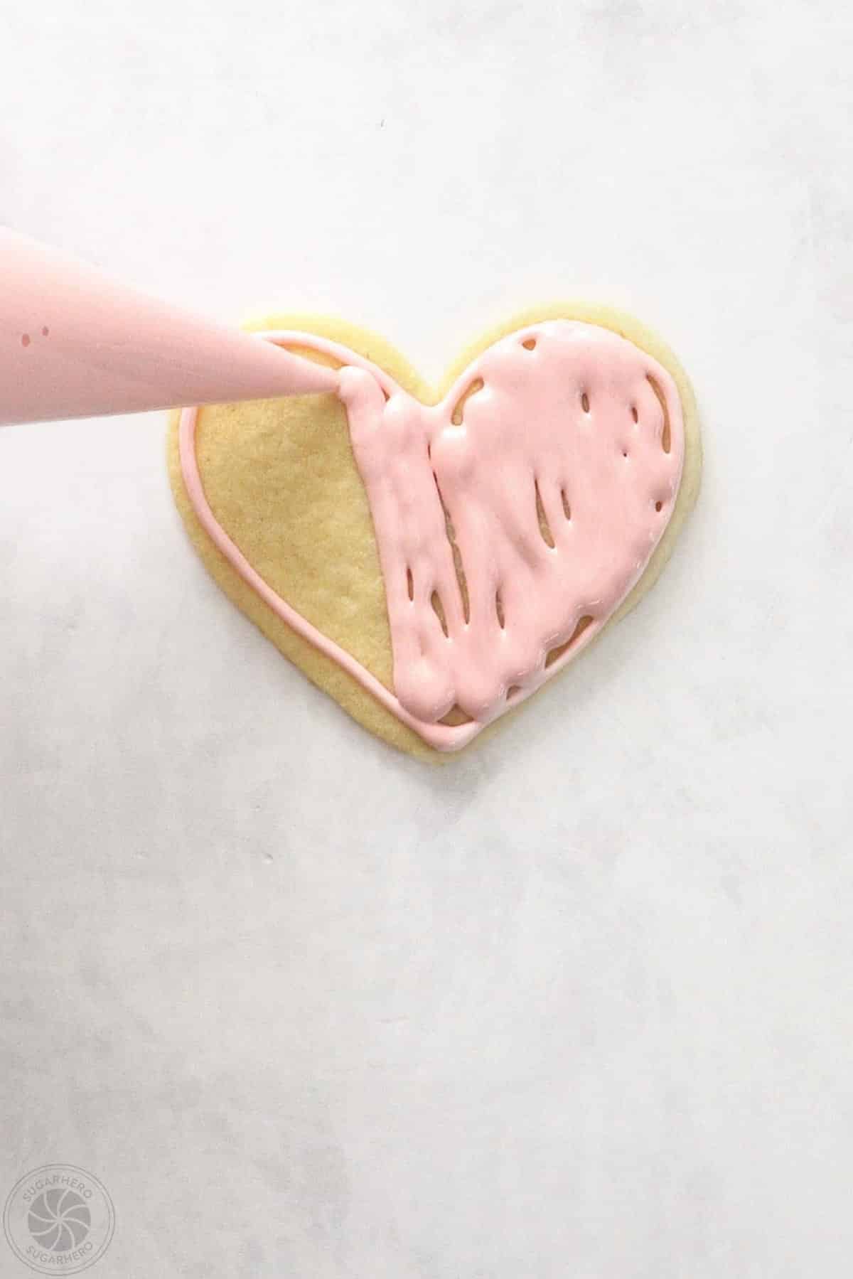Hand piping royal icing in the center of an outlined sugar cookie.
