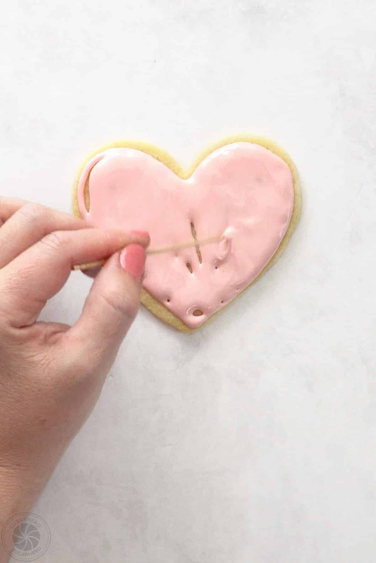 Hand using a toothpick to finish flooding the top of a sugar cookie.
