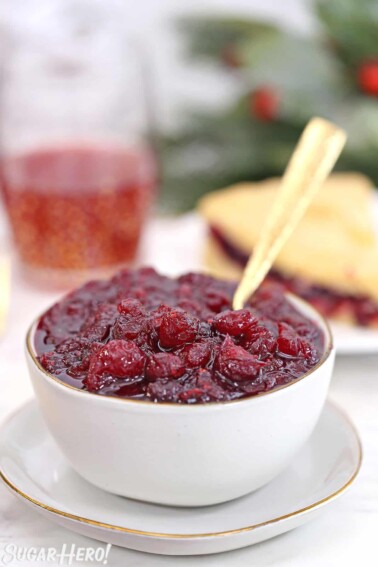 Homemade cranberry sauce in a white bowl with a gold spoon sticking out.
