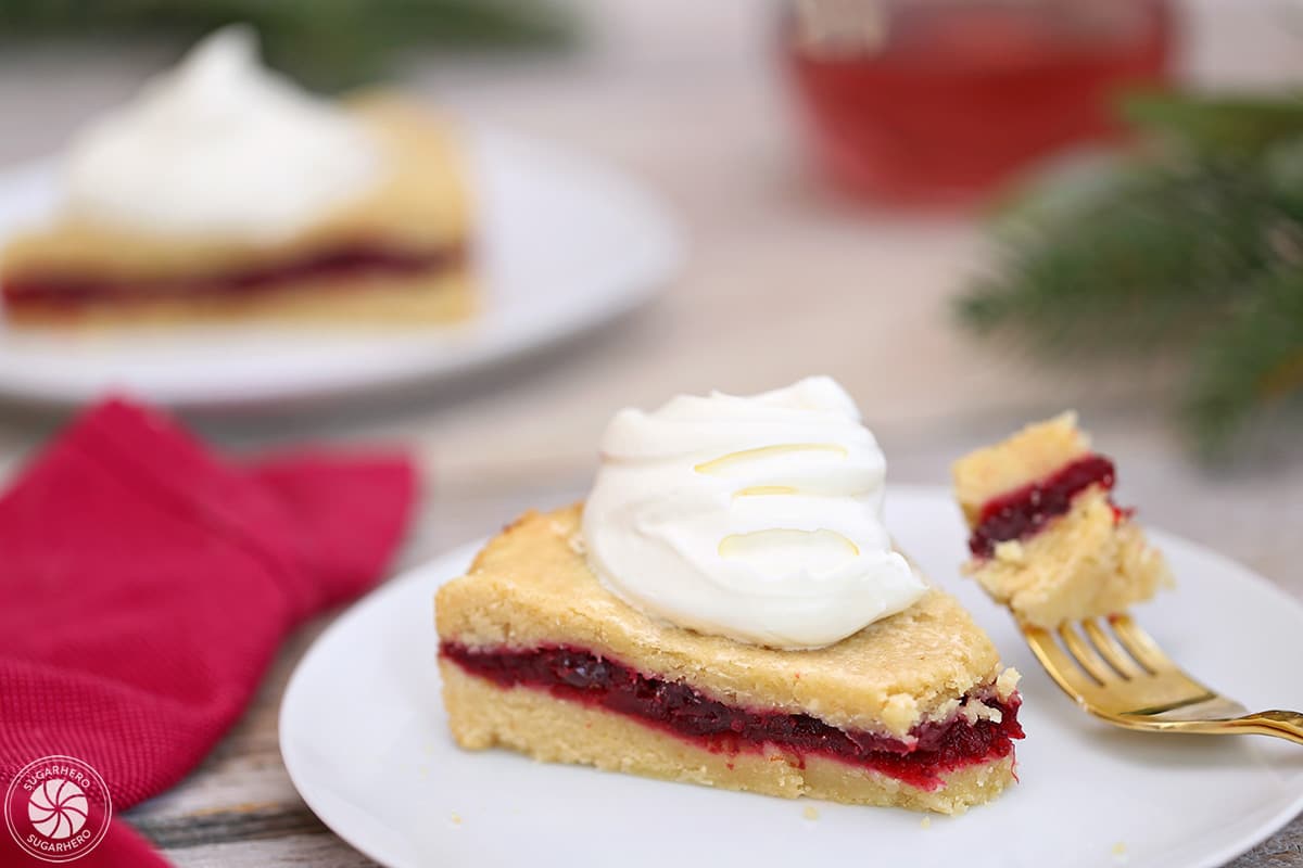 Slice of Cranberry Sauce Cake on a white plate, with a bite taken out by a gold fork.