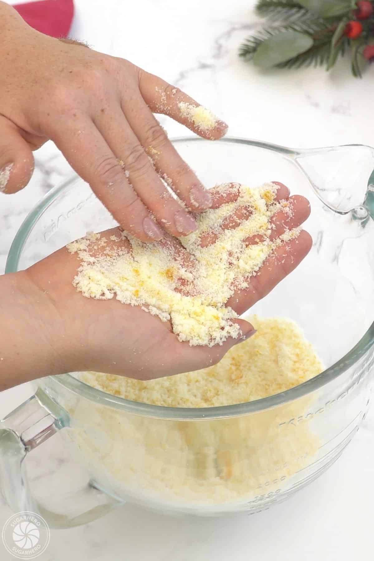 Rubbing together orange zest and sugar over a clear mixing bowl.