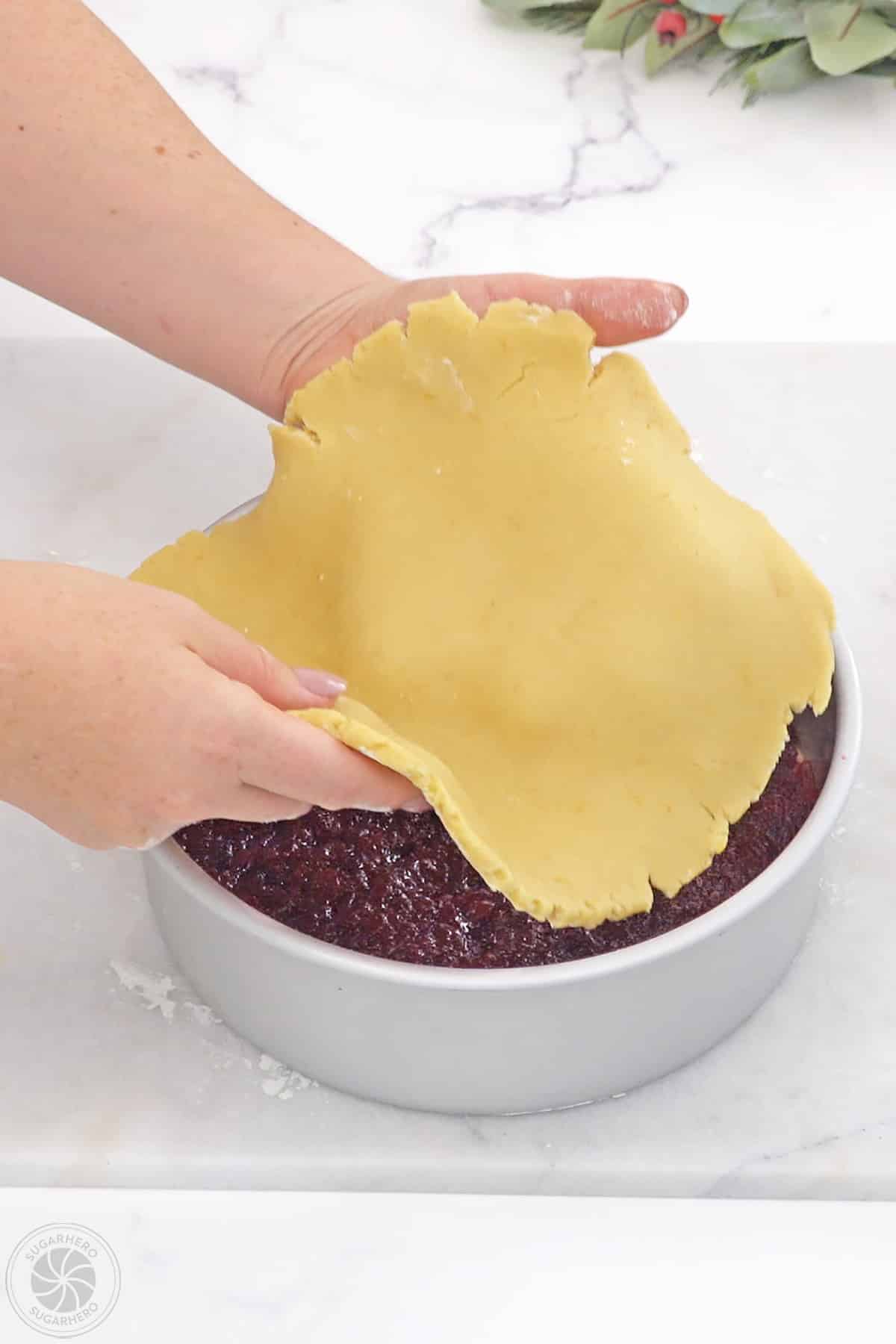 Hands placing the top cake layer over the cranberry filling.