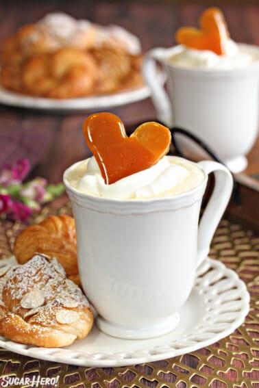 Mug of Crème Brulee White Hot Chocolate on a white plate next to pastries.
