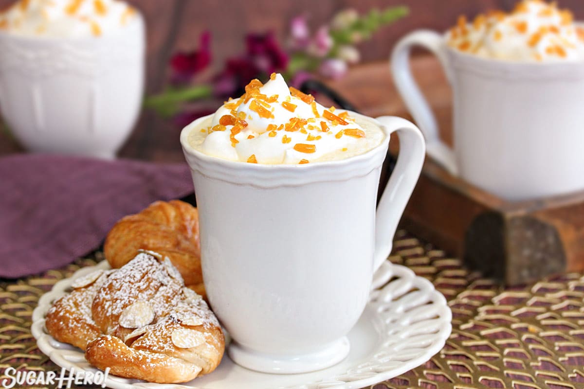 Mug of Cr&egrave;me Brulee White Hot Chocolate on a white plate next to pastries.