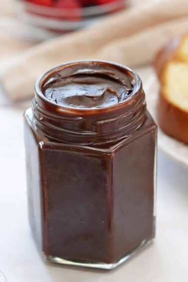 A glass jar of Chocolate Spread next to fruit and bread.