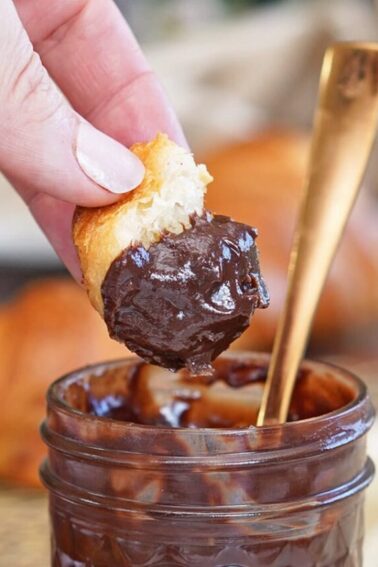Hand dipping a croissant into a jar of Coconut Chocolate Spread.