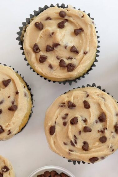 Overhead shot of six cupcakes frosted with Cookie Dough Frosting and mini chocolate chips scattered on top.