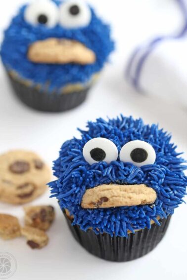 Two Cookie Monster Cupcakes with a white and blue napkin and crumbled cookies on the side.