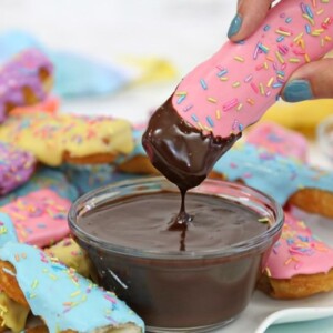 A pink glazed Doughnut Dipper being dipped in a small bowl of mocha sauce.