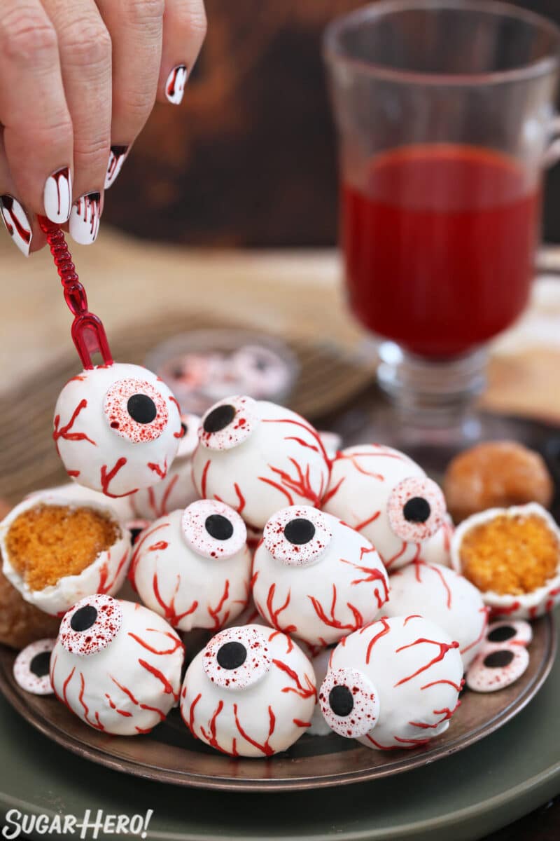 Hand holding a red appetizer fork with a Donut Hole Eyeball on it.