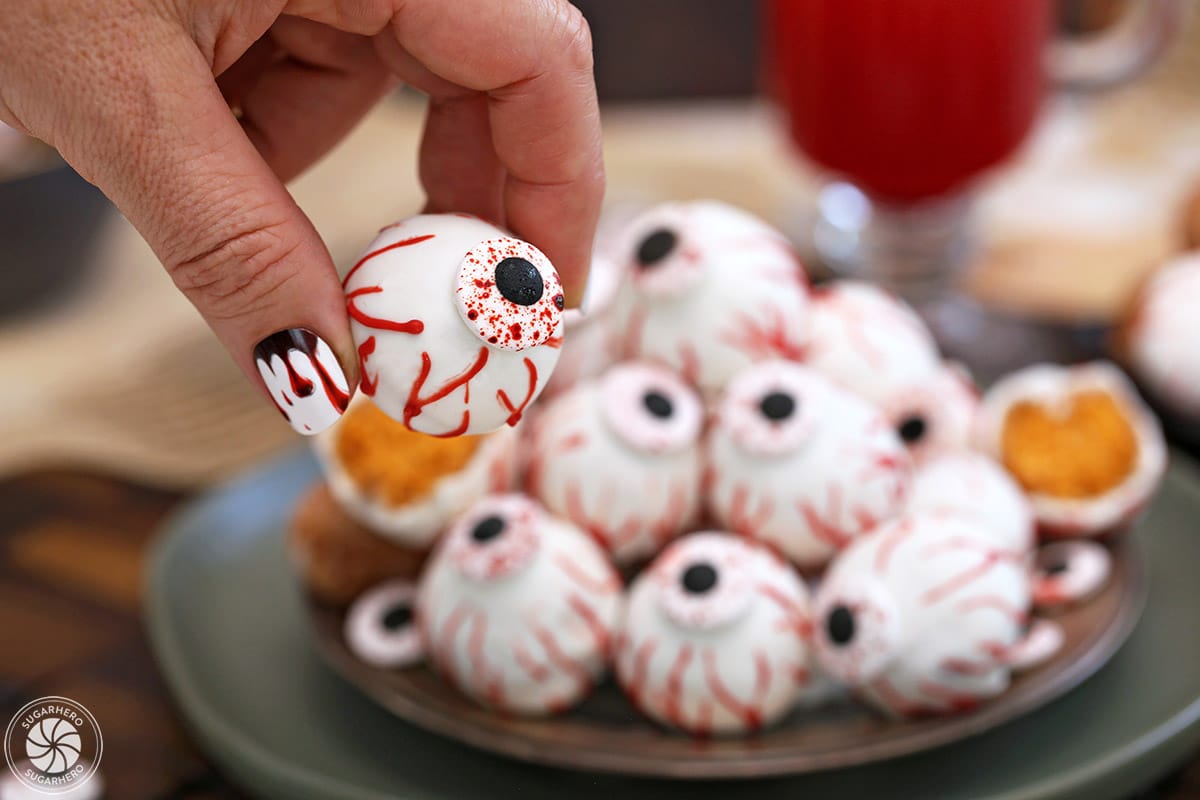 Hand with dripping blood manicure holding a Donut Hole Eyeball up to the camera.