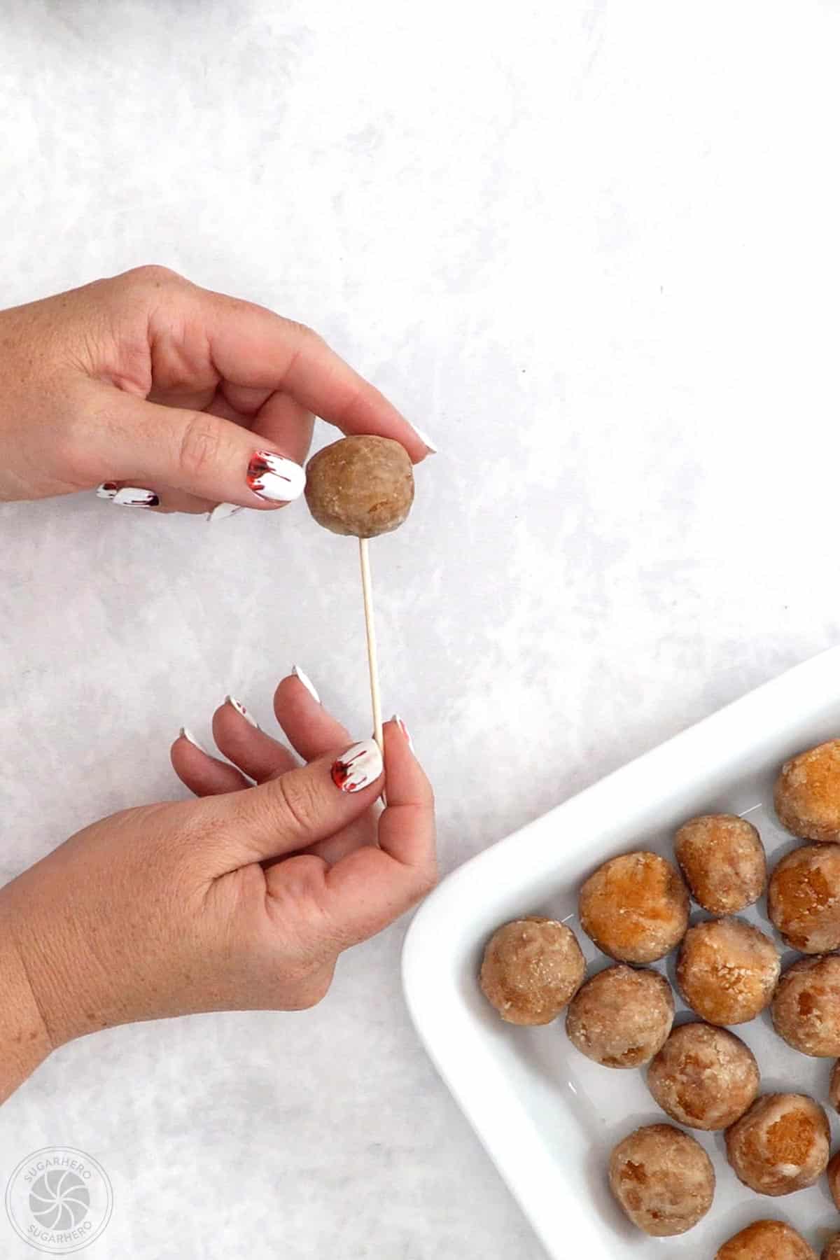Hand inserting a long toothpick into a donut hole.