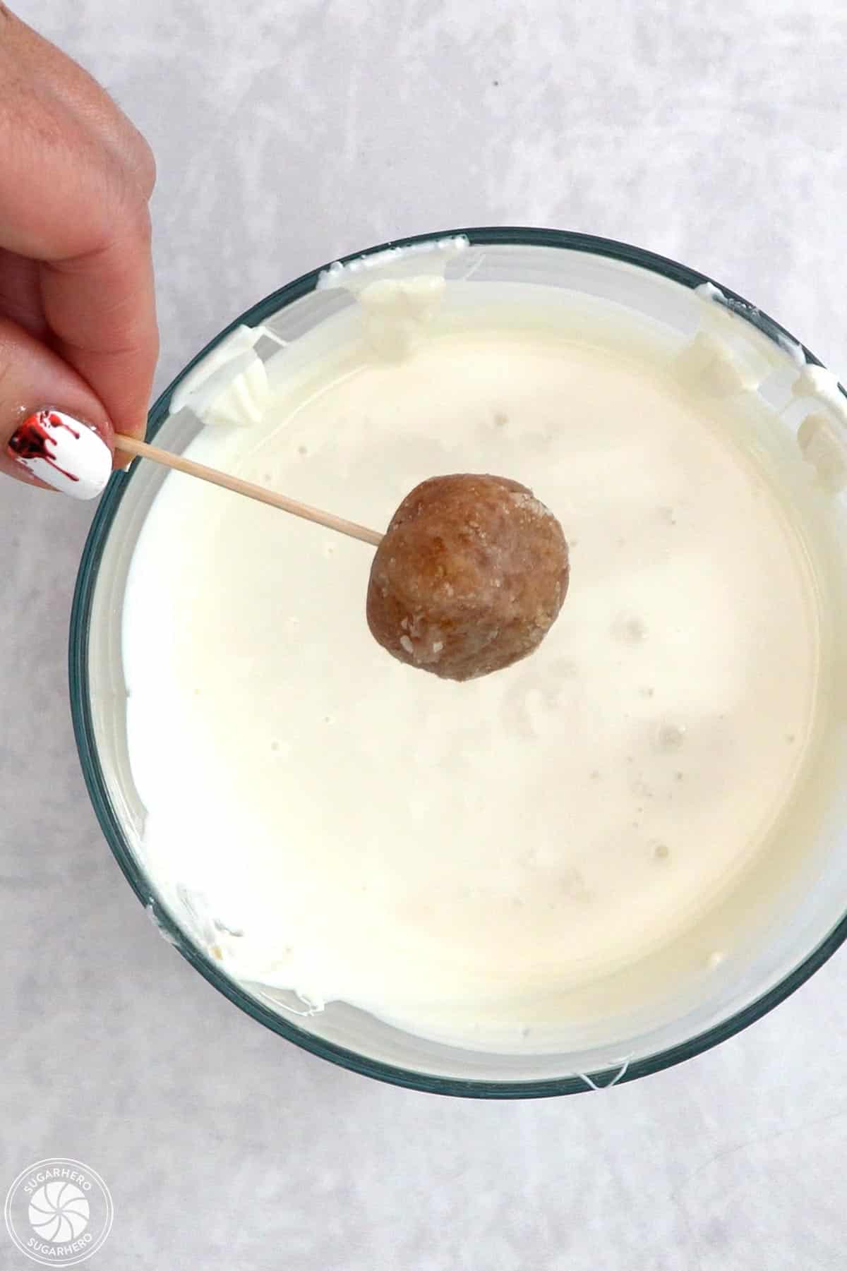 Hand holding a picked donut hole and getting ready to dip it in warm white candy coating.