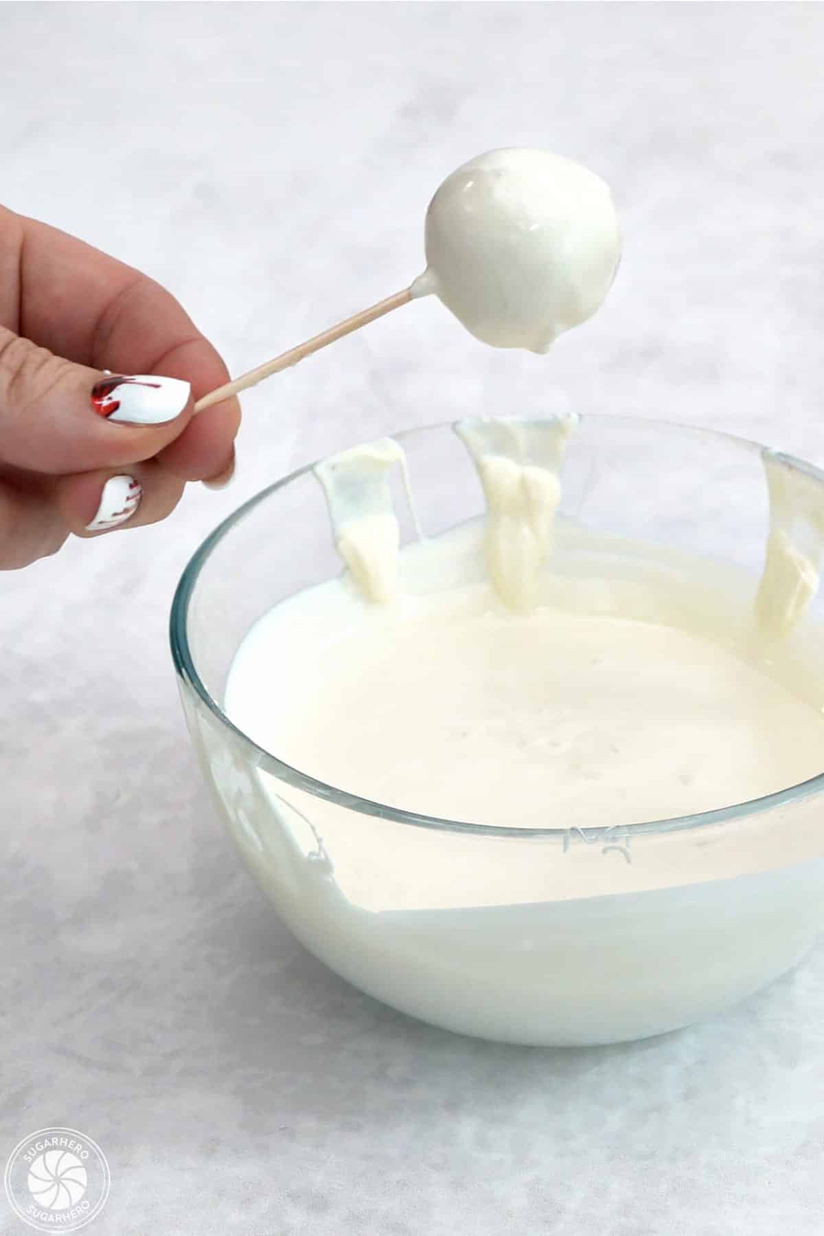 Hand holding a picked donut hole that has been dipped in white candy coating.