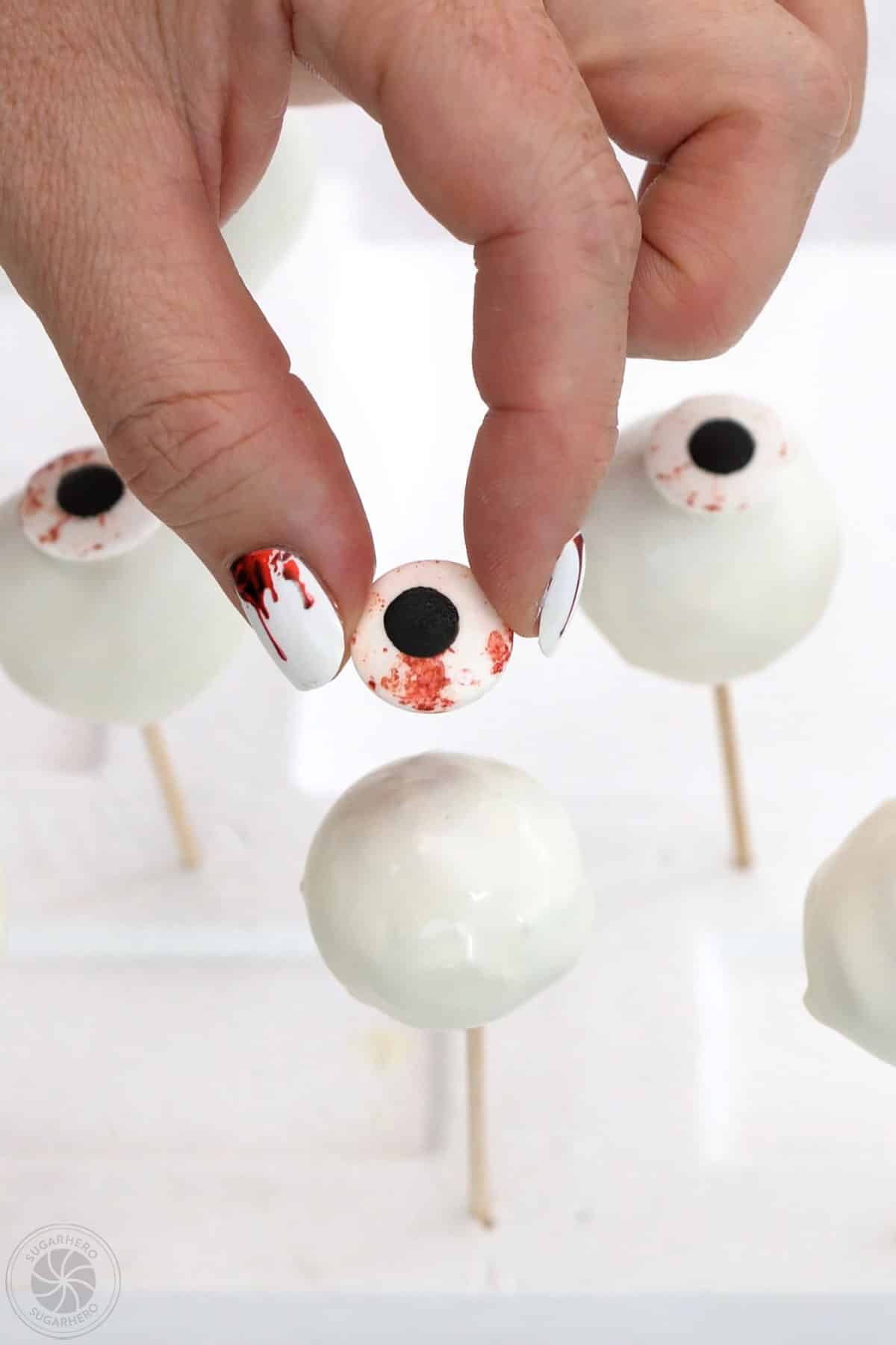 Hand placing a blood stained candy eyeball on top of a dipped donut hole.