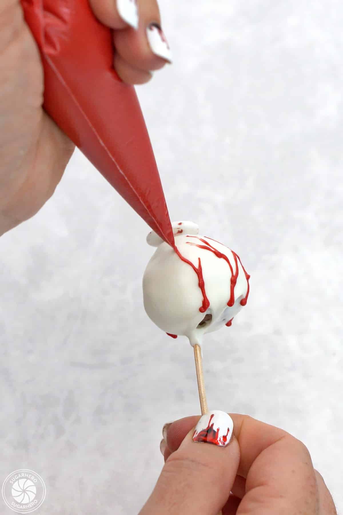 Hand piping red candy coating on dipped donut holes to look like blood vessels.
