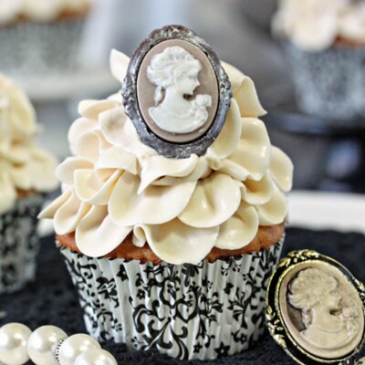 Close up of an Earl Grey Lavender Cupcake next to a broch and pearls.